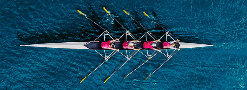 Neljä punapaitaista kilpasoutajaa merellä, kuvattu yläpuolelta.